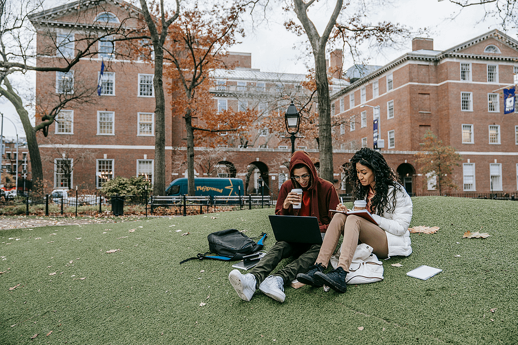 college students sitting on the grass in front school studying